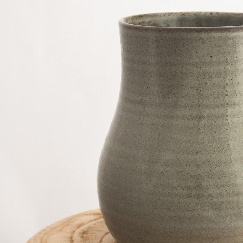 Close up of a Robert Gordon pottery botanica banksia grey vase sitting on a natural wooden round side table