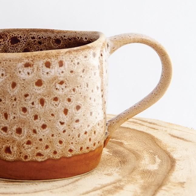 Close up of a Robert Gordon white ochre organic mug coffee cup sitting on a natural wooden round side table