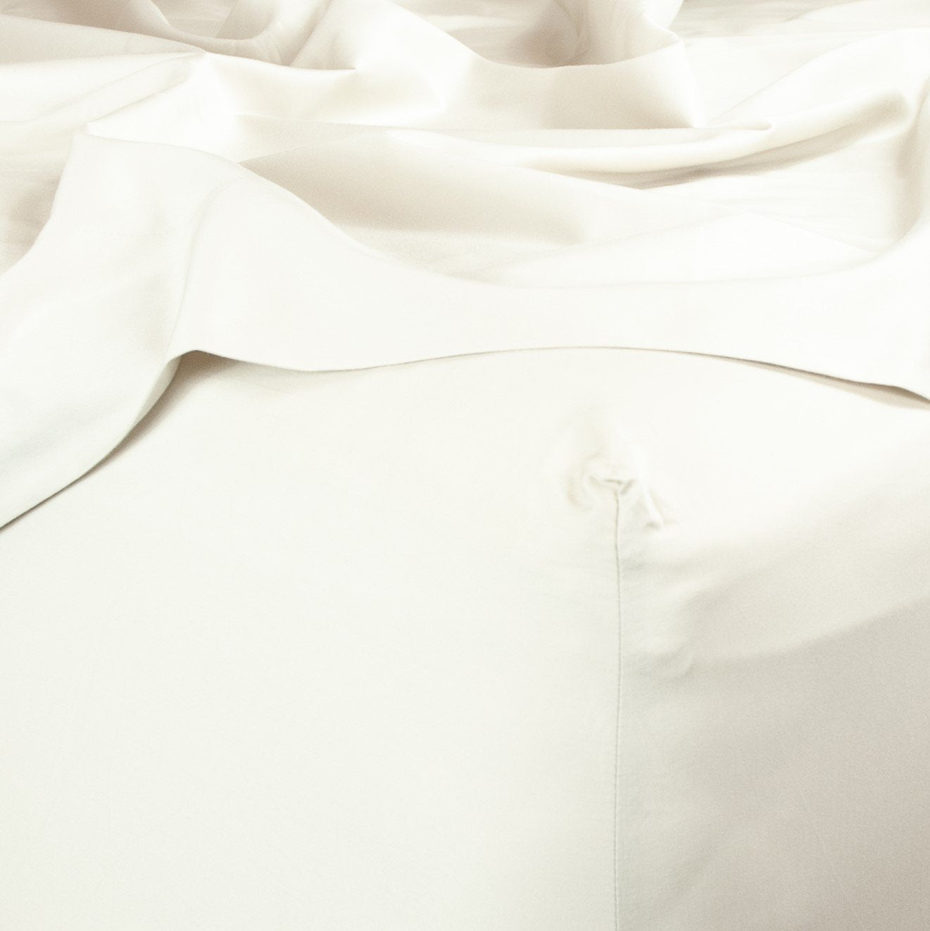 Corner of bed with organic cotton fitted sheet and top sheet in warm white