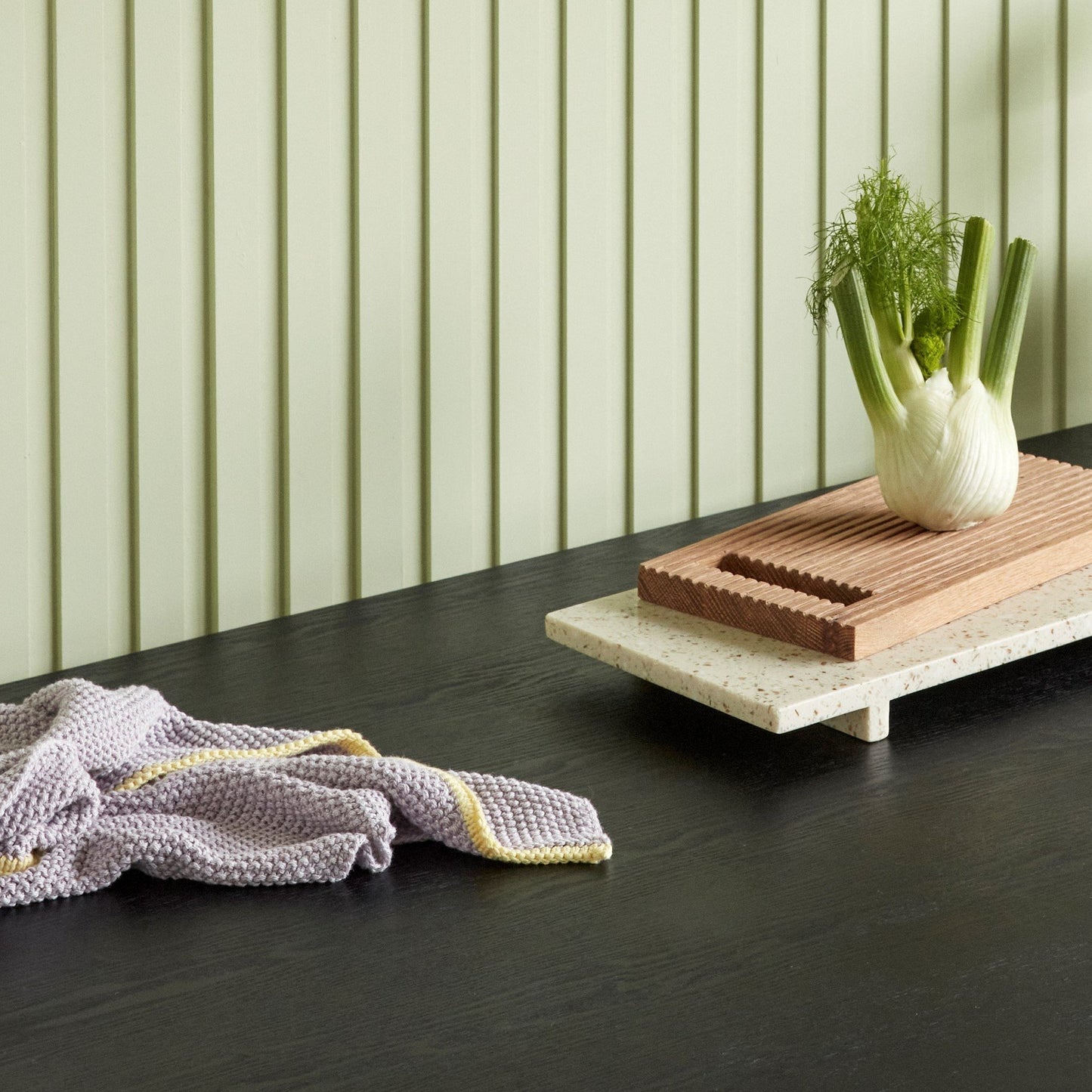 Hubsch Interior Scandi designer tea towel in lilac purple and yellow cotton knit lying on a kitchen bench with a wooden board